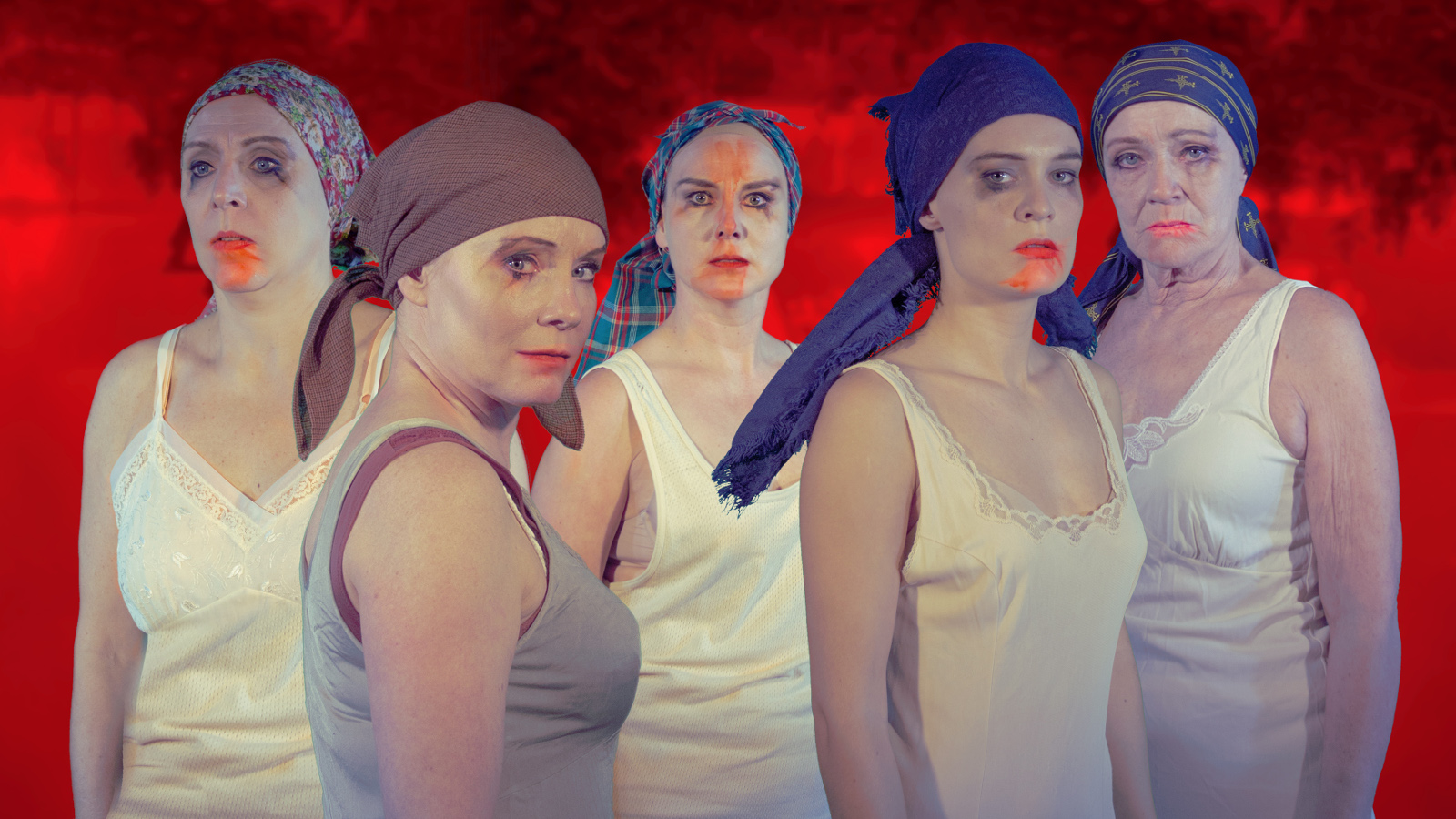 Kuvassa on viisi naista, joilla tiukat huivit päässään ja vaaleat hihattomat paidat päällään.Heillä on punaista huulipunaa.