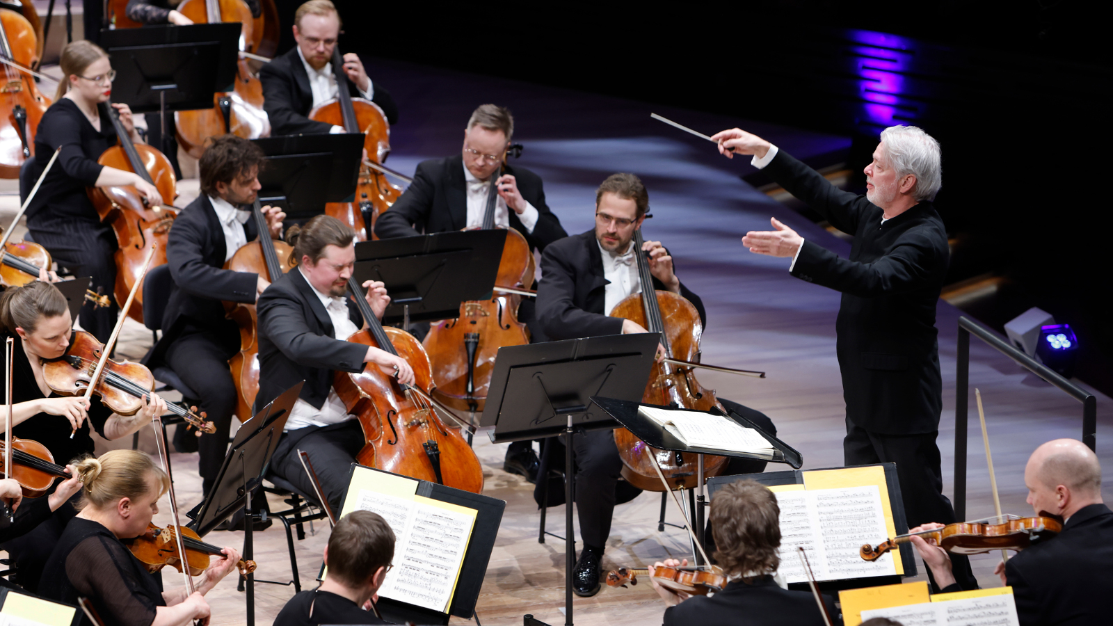 Kuvassa on Jukka-Pekka Saraste johtamassa Helsingin kaupunginorkesteria.  Kuva on otettu yläviistosta ja sivusuunnassa. 