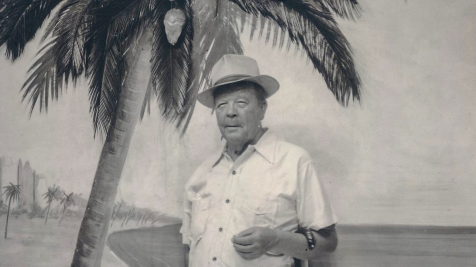 Kuvassa on Juho Rissanen seisomassa palmun luona. Kuvan sävy on harmahtava.