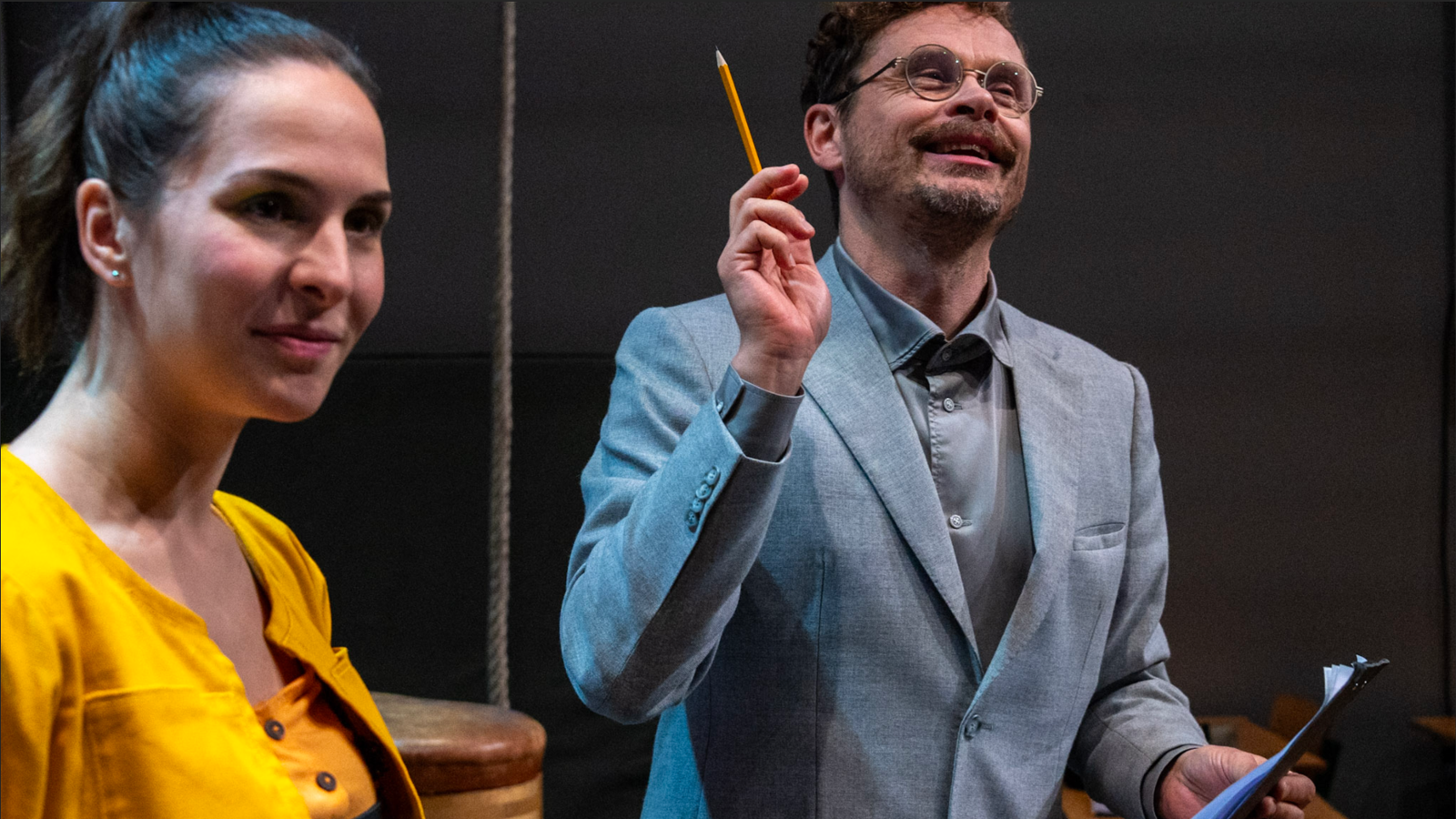 Kuvassa on Jussi Lehtonen opettajana harmaassa takissa ja osoittaa ylöspäin kynä kädessään.  Vasemmalla on Denisa Snyder keltaisessa puserossa  ja katsoo vinosti oikealle.