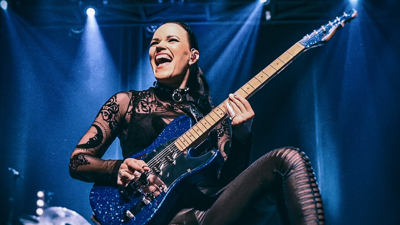 Kuvassa on Erja Lyytinen soittamassa kitaraa ja kuva on otettu yläviistoon.  Hänellä on musta läpikuultava puku, jossa on kukallista ja ruotomaista kuviointia. Kuvan sävy on tumman sininen sävy ja taustalla on kohdevaloja.