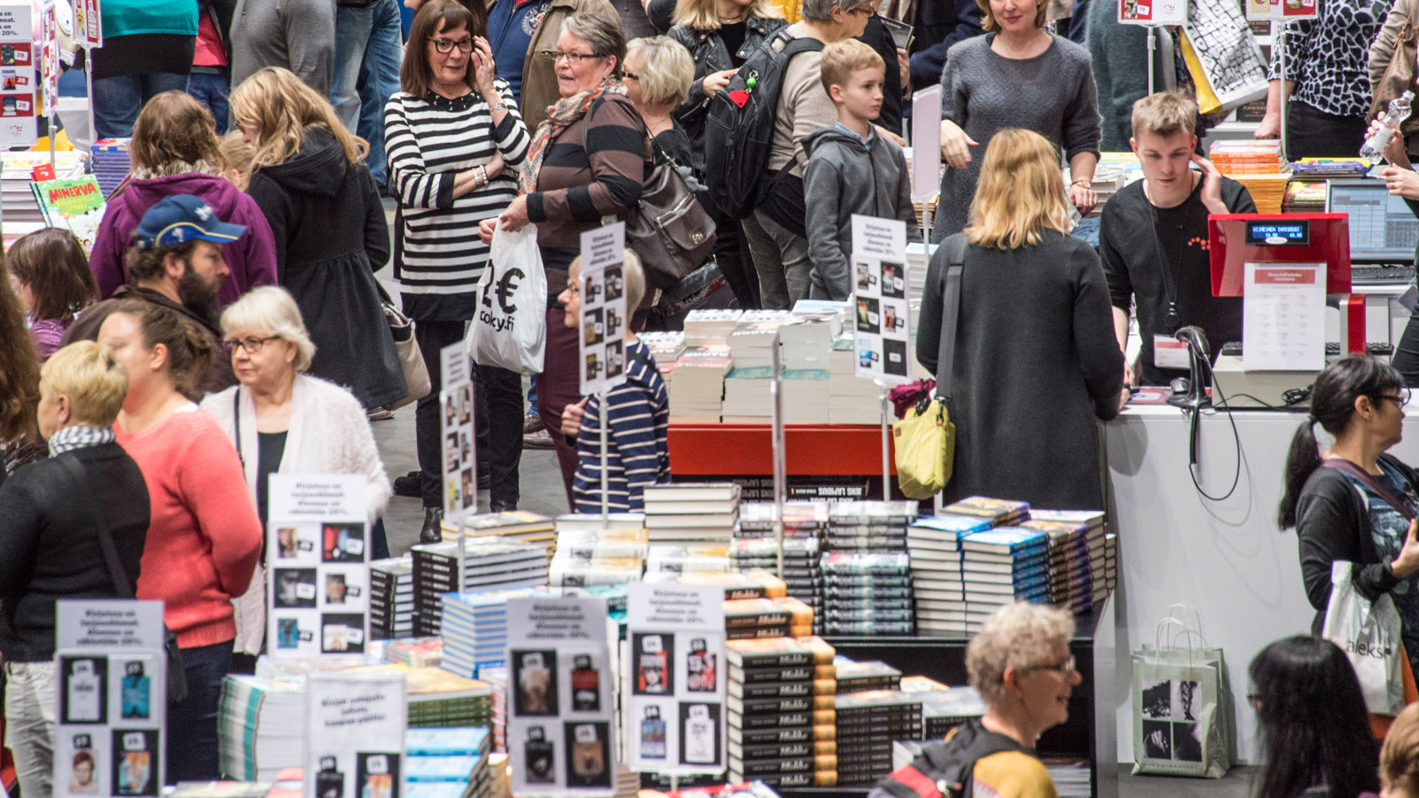 Kuvassa on ihmisiä katselemassa kirjoja, joita on isolla pöydällä Kirjamessuilla Messukeskuksessa.