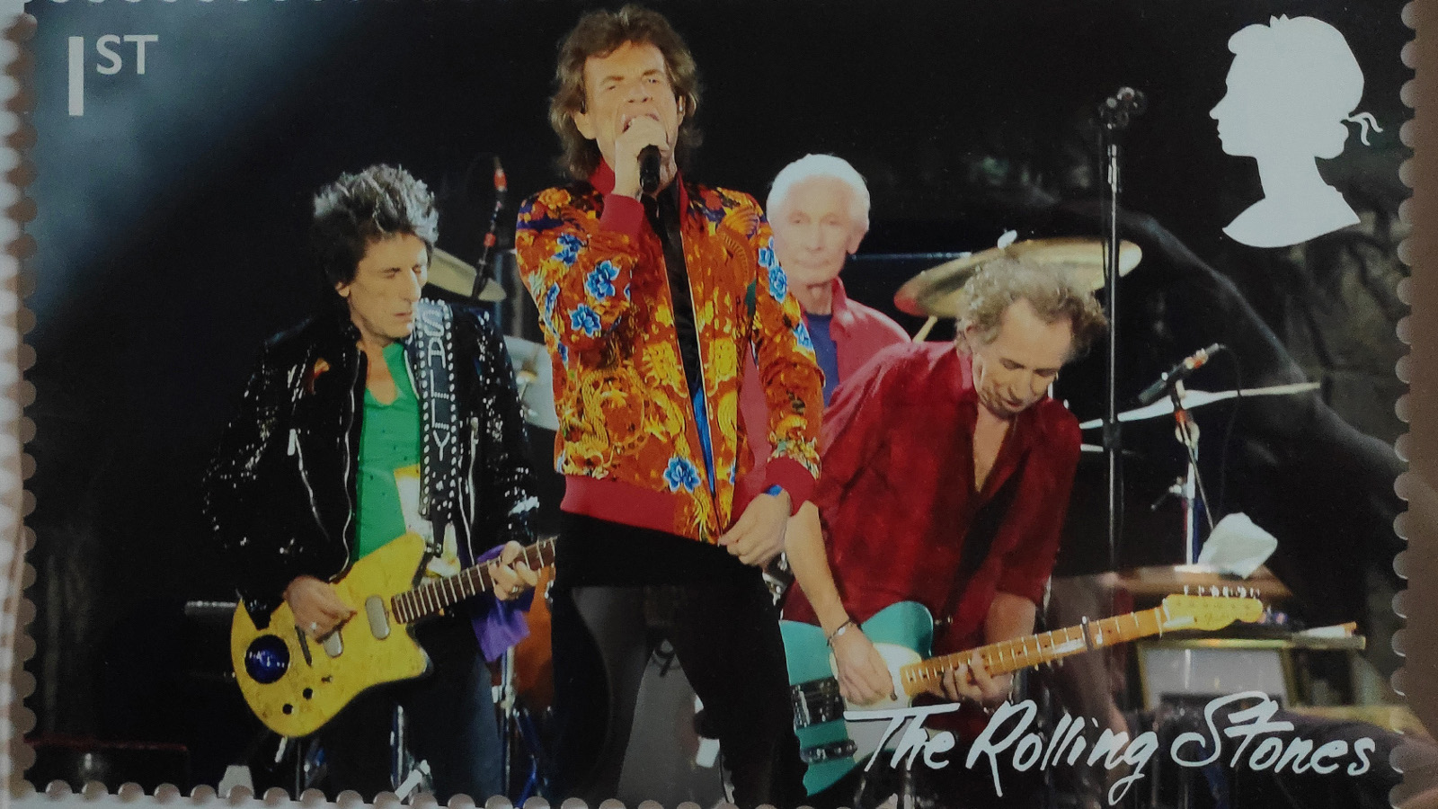 Kuvassa on Rolling Stones -yhtyeen postimerkki. Siinä ovat kitaristit takana ja edessä Keith Richards laulamassa mikin kanssa. Hänellä on punainen takki päällään.  