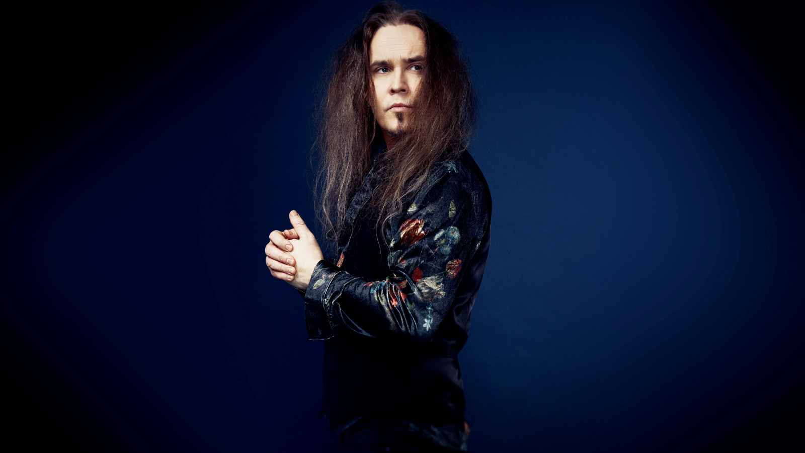 Kuvassa on Jarkko Ahola kääntyneenä sivuttain vasemmalle ja katse käännettynä oikealle. Hänellä on musta nahkatakki ja tausta on tumman sininen. Aholalla on pitkät, ruskeat hiukset.