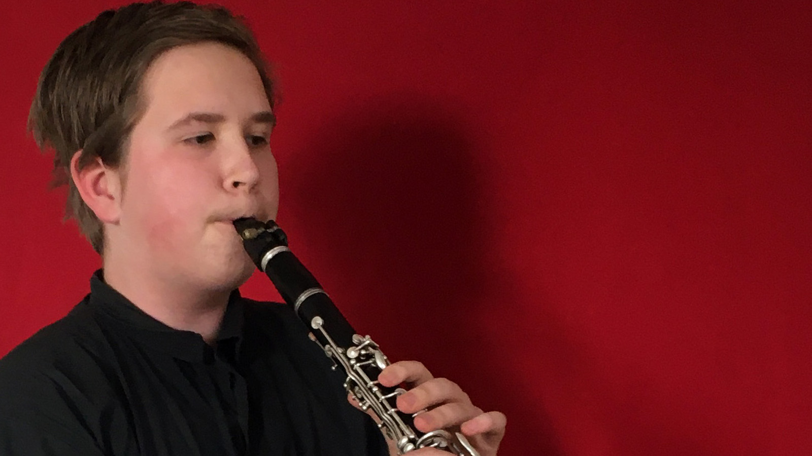 Kuvassa on Joonatan Henriksson kasvokuvassa ja hän soittaa klarinettia. Hänellä on musta paita päällään ja tausta on punainen.