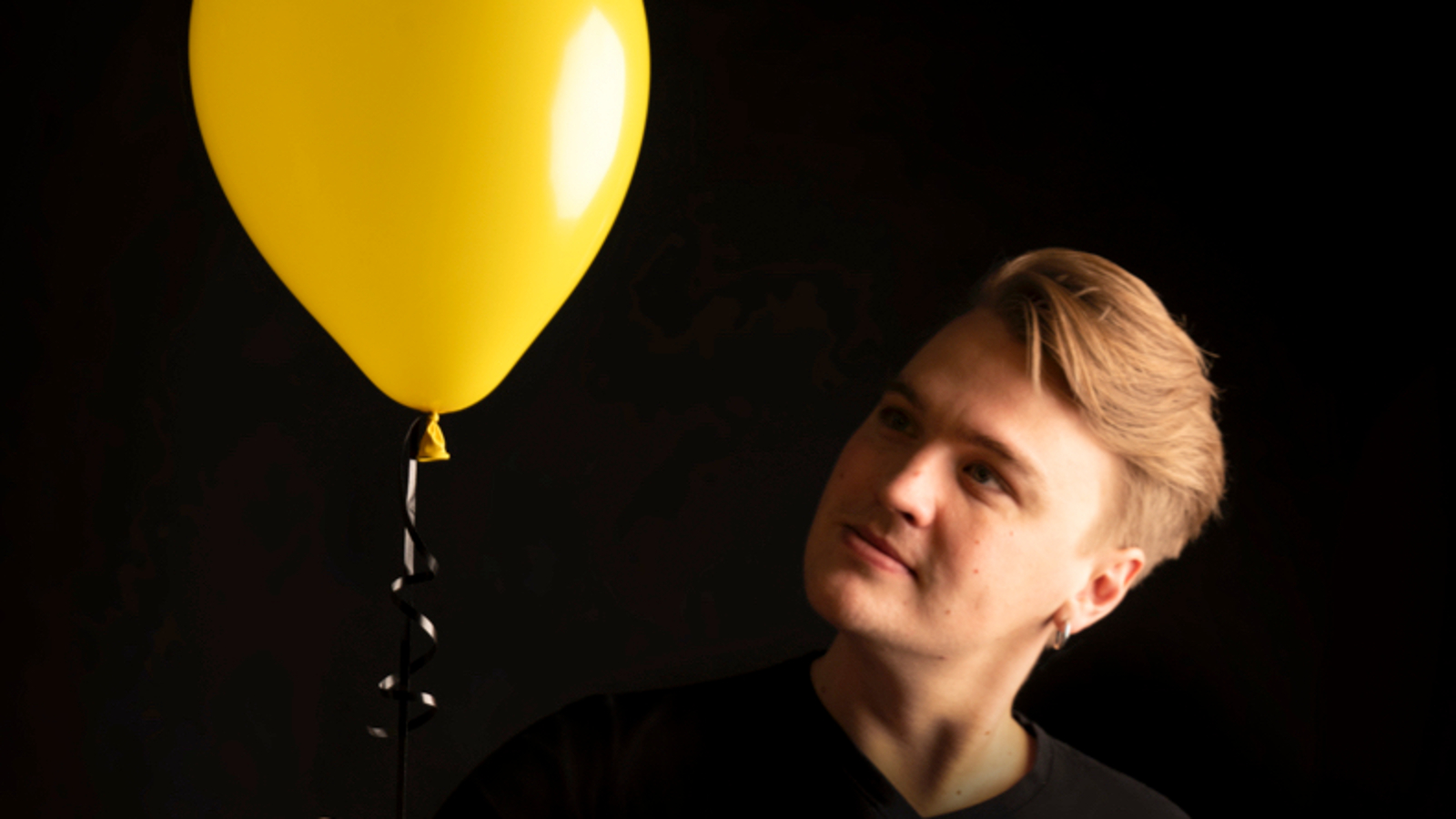 Kuvassa ovat Roope Mäenpään kasvot oikealla ja hän pitelee keltaista ilmapalloa, joka on vasemmalla yläviistossa.