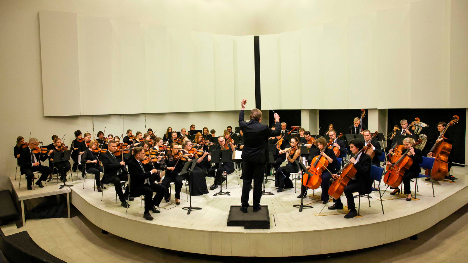 Kuvassa on Tampereen sinfoniaorkesteri kaaressa esiintymislavalla, joka on vaaleaa puuta.
