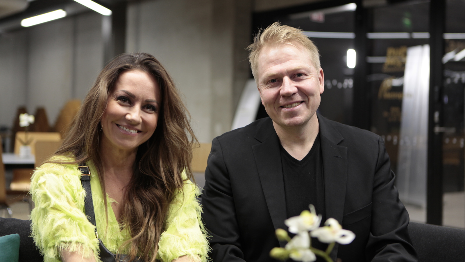 Kuvassa ovat puolivartalokuvassa vasemmalla Jaana Pelkonen vaalean vihreässä röyhelöisessä mekossa ja Aki Riihilahti mustassa t-paidassa ja takissa.