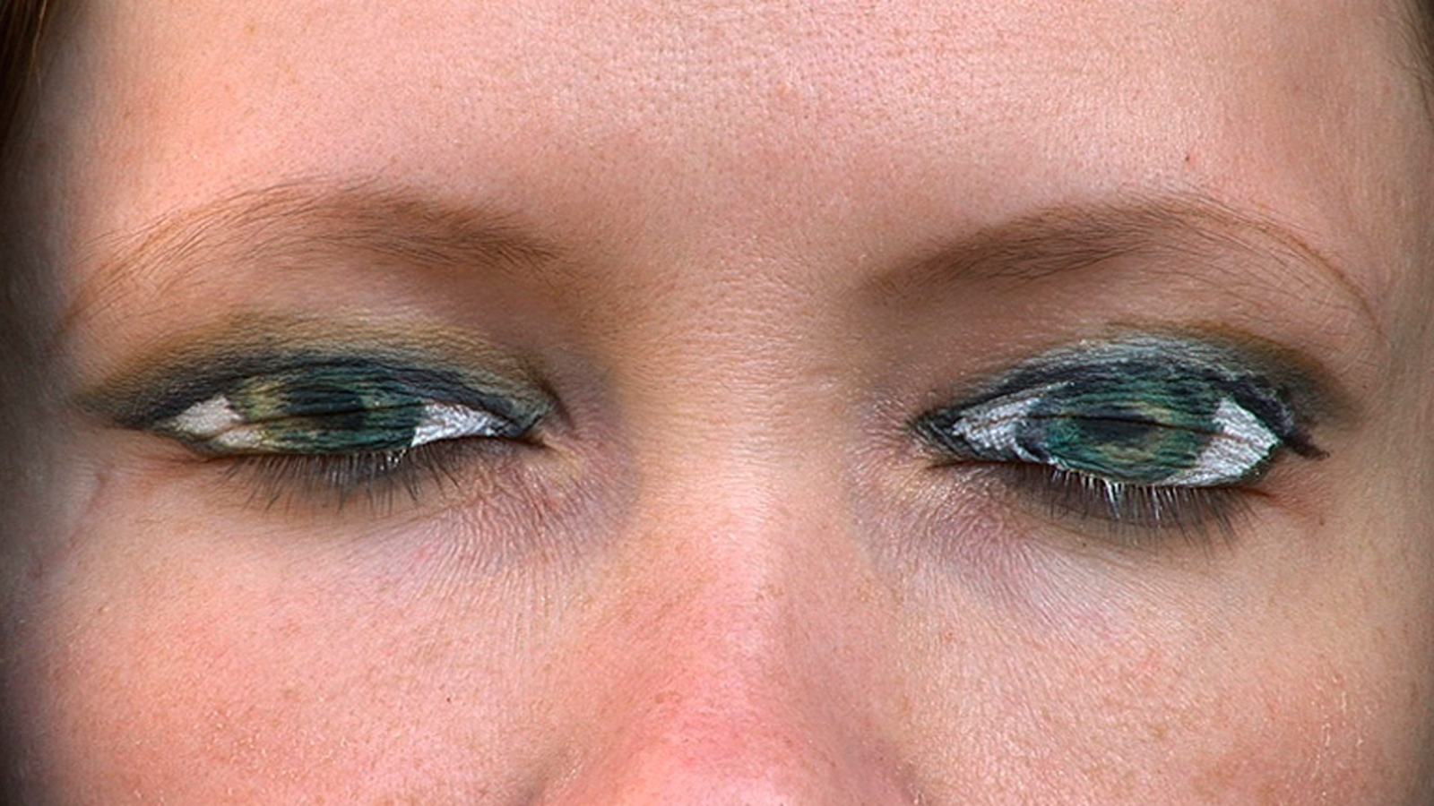 Kuvassa on naisen kasvoista silmät tiukalla rajauksella. Silmät ovat siniset ja niissä on heijastuksia.