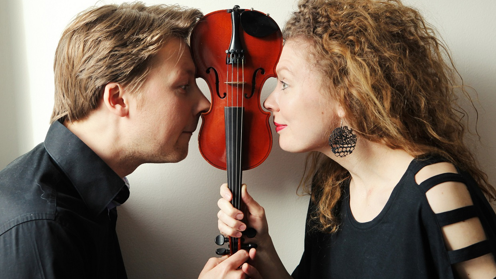 Kuvassa ovat Antti Tikkanen v. Takaa asemmalla ja Minna Pensola oikealla puolivartalokuvassa.  He pitävät välissään käsissään viulua varresta kiinni ylösalaisin.