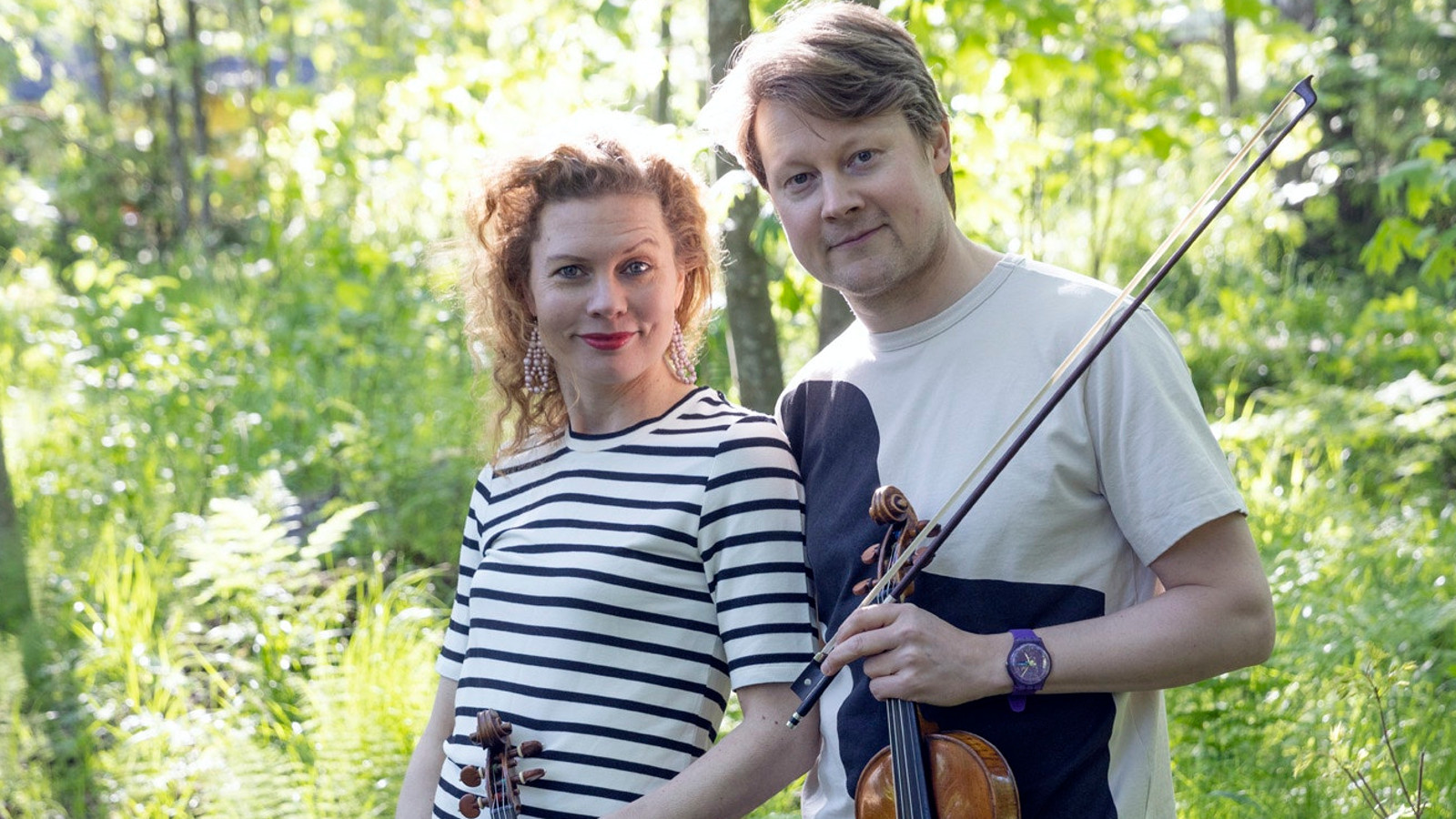 Kuvassa ovat Minna Pensola musta-valko raidallisessa puserossa ja Antti Tikkanen valkoisessa t-paidassa viulu kädessään.  He ovat lehtomaisessa, vihreässä metsässä.