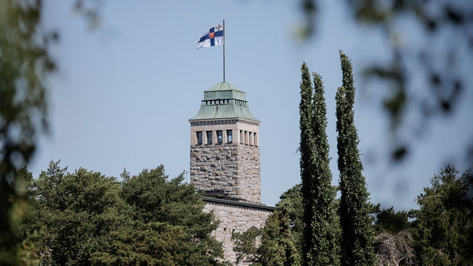 Kuvassa on Kultarannan päärakennuksen yläosan torni harmaasta kivestä.  Siinä liehuu Suomen virallinen lippu. Kuva on kesäkuva ja vieressä oikealla korkeita tuijia. Vasemmalla matalampia lehtipuiden latvoja.