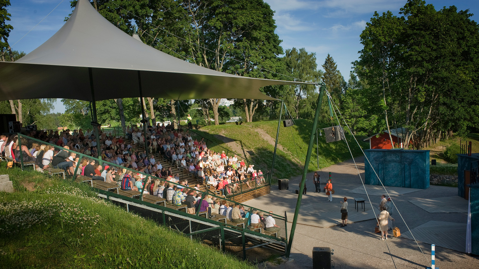 Kuvassa on Lappeenrannan kesäteatteri vihreässä rinteessä ja alhaalla on hiekkakenttää, jossa on teatteriin tulijoita.