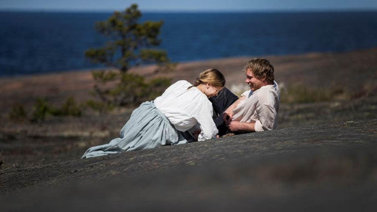 Kuvassa ovat Amanda Jansson ja Linus Troedsson makailemassa rantakalliolla meren äärellä.  Jansson on kääntyneenä Troedssonin suuntaan ja hänellä on valkoinen pusero ja vaalean sininen hame päällään. 