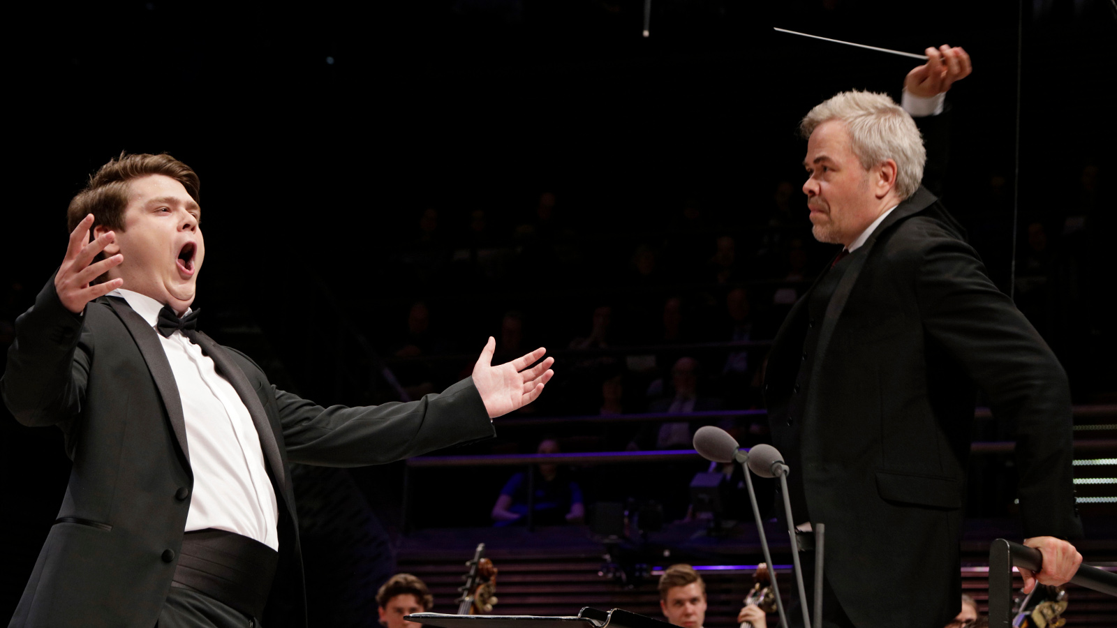 Kuvassa Stefan Astakhov kädet ojennettuina vasemmassa reunassa ja oikealla Hannu Lintu johtamassa orkesteria oikealla oikea käsi ylhäällä tahtipuikko kädessään. Alhaalla on orkesteri.