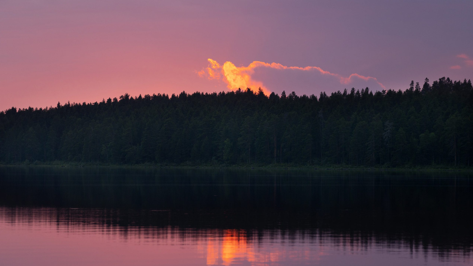 Kuvassa on Lammasjärvi, jossa näkyy tummaa metsää järvenn takana ja se heijastuu järveen. Taivas on punertavan violetin värinen ja takana on keltainen sakarapilvi, joka myös heijastuu veteen.