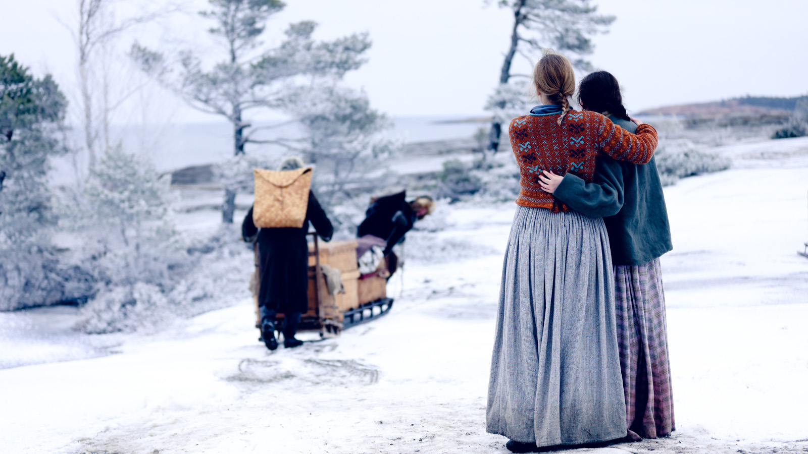 Kuvassa on kaksi naista selin pitkissä hameissa, mies lähtee rekeä työntäen kohti jäistä merta. Maassa on lunta.