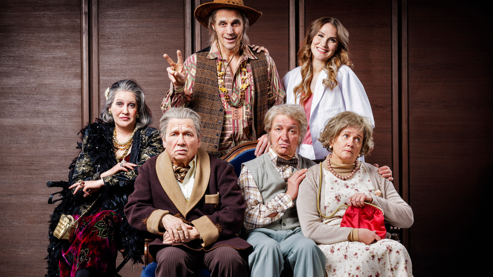 Kuvassa on neljä näyttelijää alarivissä istumassa ja kaksi ylärivissä seisomassa. He ovat vanhojen ihmisten vaatteissa.