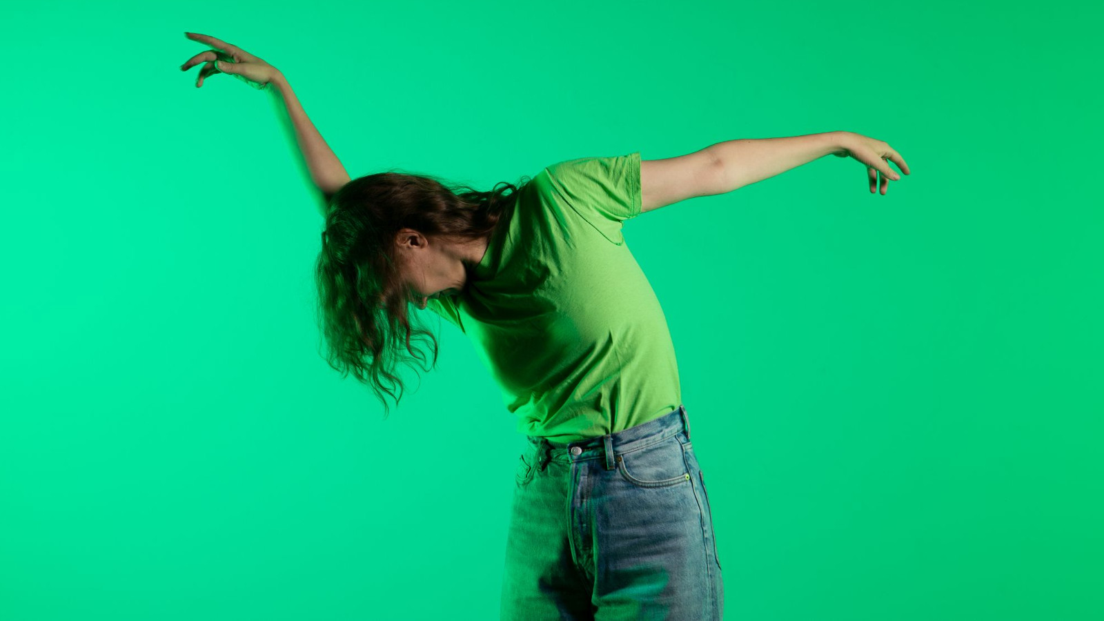 Kuvassa on vihreällä taustalla Liisa Pentti tanssimassa puolivartalokuvassa. Hänellä on pää alaspäin ja oikea käsi ojennettuna ylöspäin ja vasen käsi ojennettuna sivulle. Pentillä on päällään vihreä t-paita ja siniset farkut.