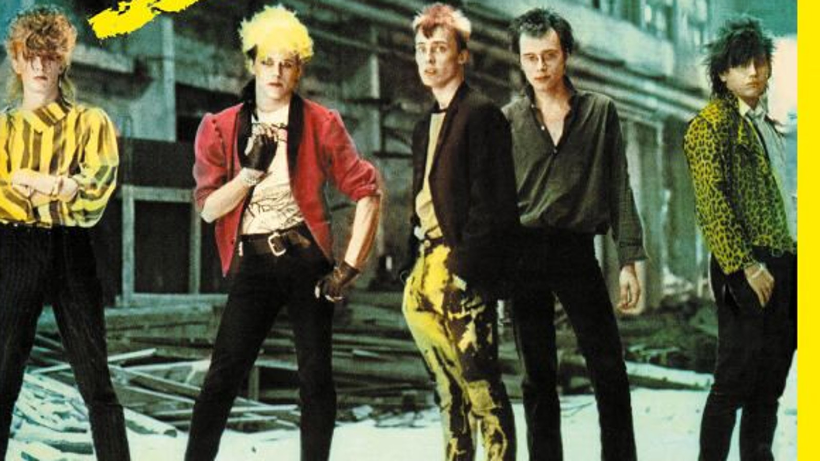 Kuvassa on Dingon viisi jäsentä seisomassa betonisen kerrostalon edessä. Heillä on mustat housut ja vasemmalla olevalla kelta-musta raitainen paita. Hänen vieressään on Neuman, jolla on punainen pusakka. 