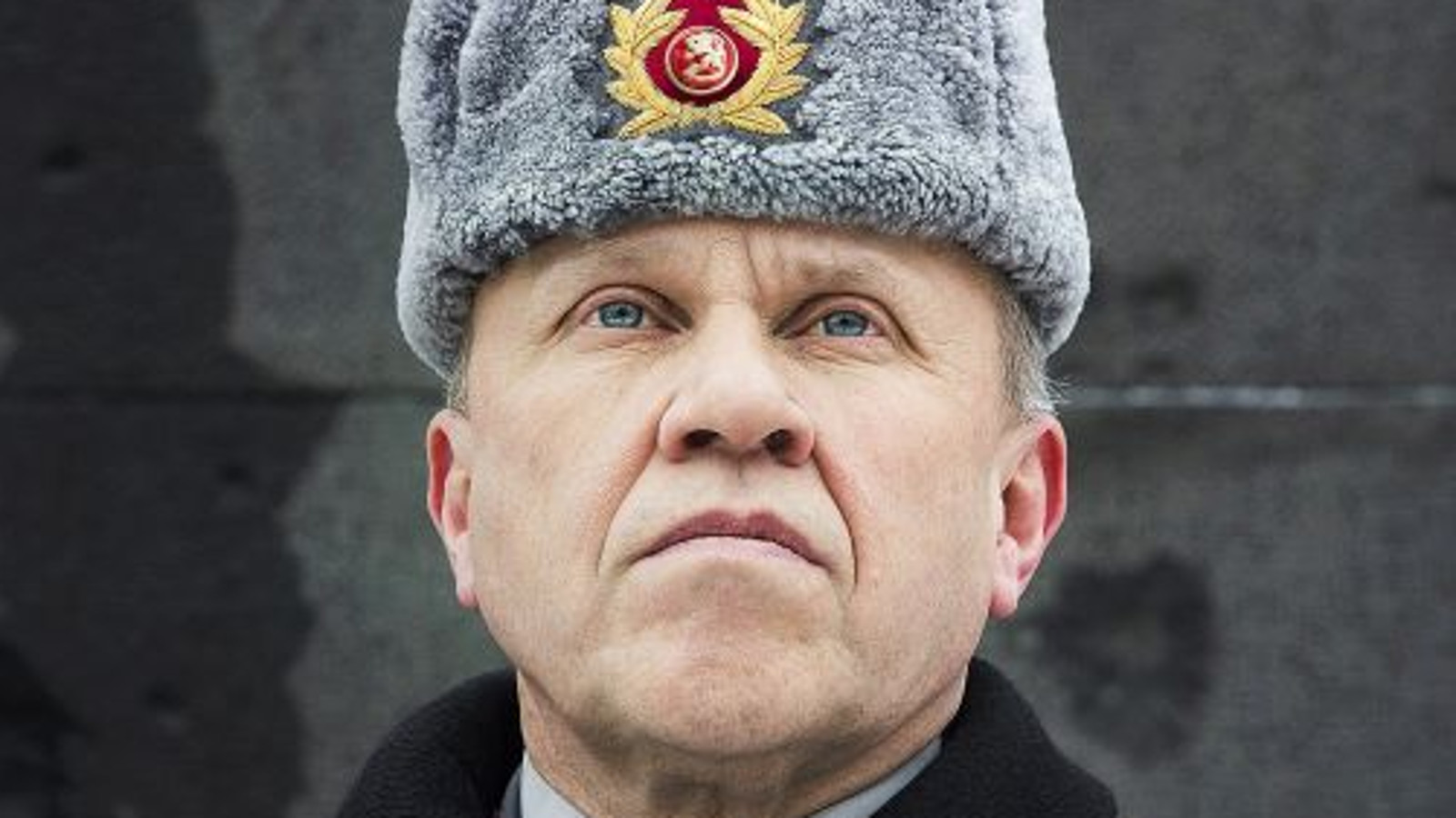 Kuvassa on Martti J. Kari kasvokuvassa ja hänellä on Suomen armeijan karvahattu, jossa on Suomen leijonan kokardi hatussa. Hattu on harmaa. Tausta on tumman harmaa.