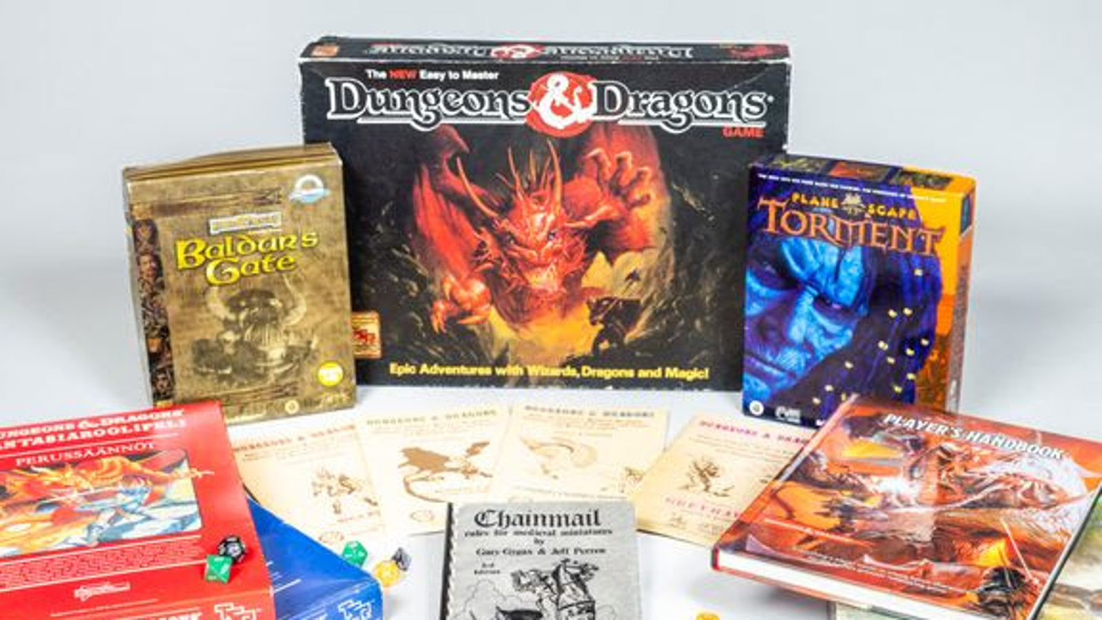 Kuvassa on keskimmäisenä Dungeons & Dragons -pelin paketti, jonka kannessa on punaisen lohikäärmeen kuva.  Ympärillä on on muita erilaisia pienempiä pelipaketteja ja pöydällä on kirjoja.