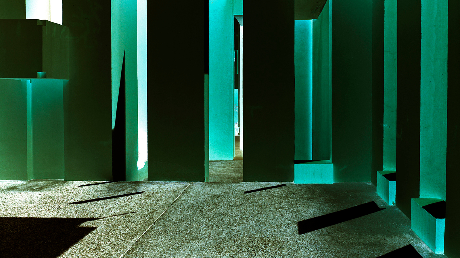 Kuvassa on Ola Kolehmaisen teos Geometric Light ja siinä on vihreitä ja mustia pylväitä  vihertävällä lattialla.  Pylväisiin osuu valoa limittäisten pylväiden väliin tulee piikkimuotoja.  Lattialla on mustaa varjoa vasemmalla.