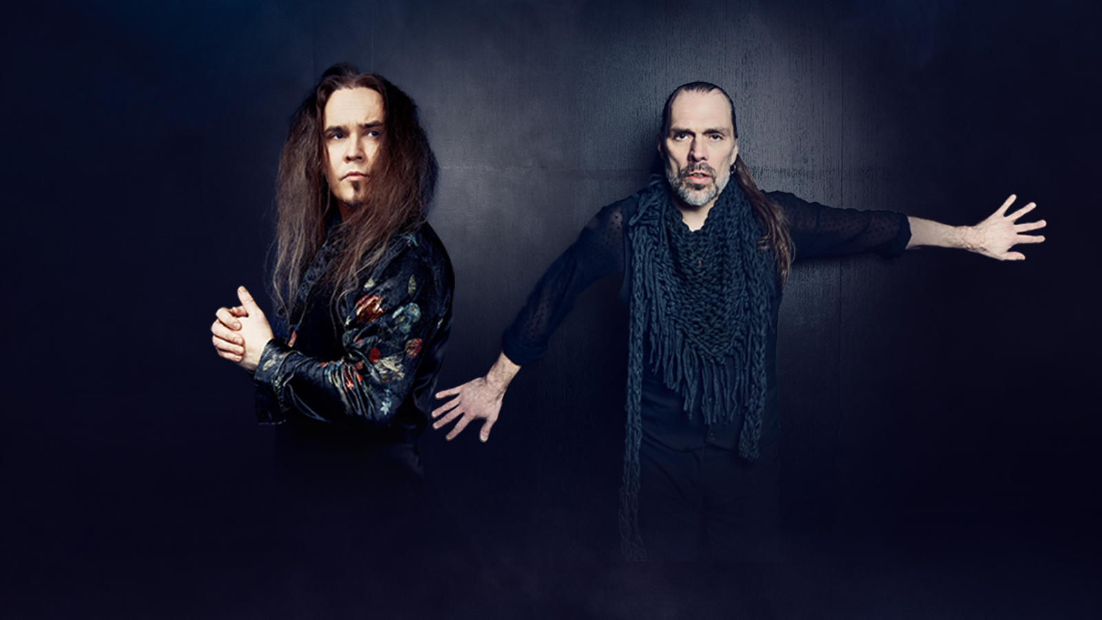 Kuvassa ovat Jarkko Ahola vasemmalla sivuttain tumman kirjavassa paidassa ja hän katsoo oikealla. Oikealla on JP Leppäluoto ja hänellä on molemmat kädet suoraan sivulla. Tausta on tumma.
