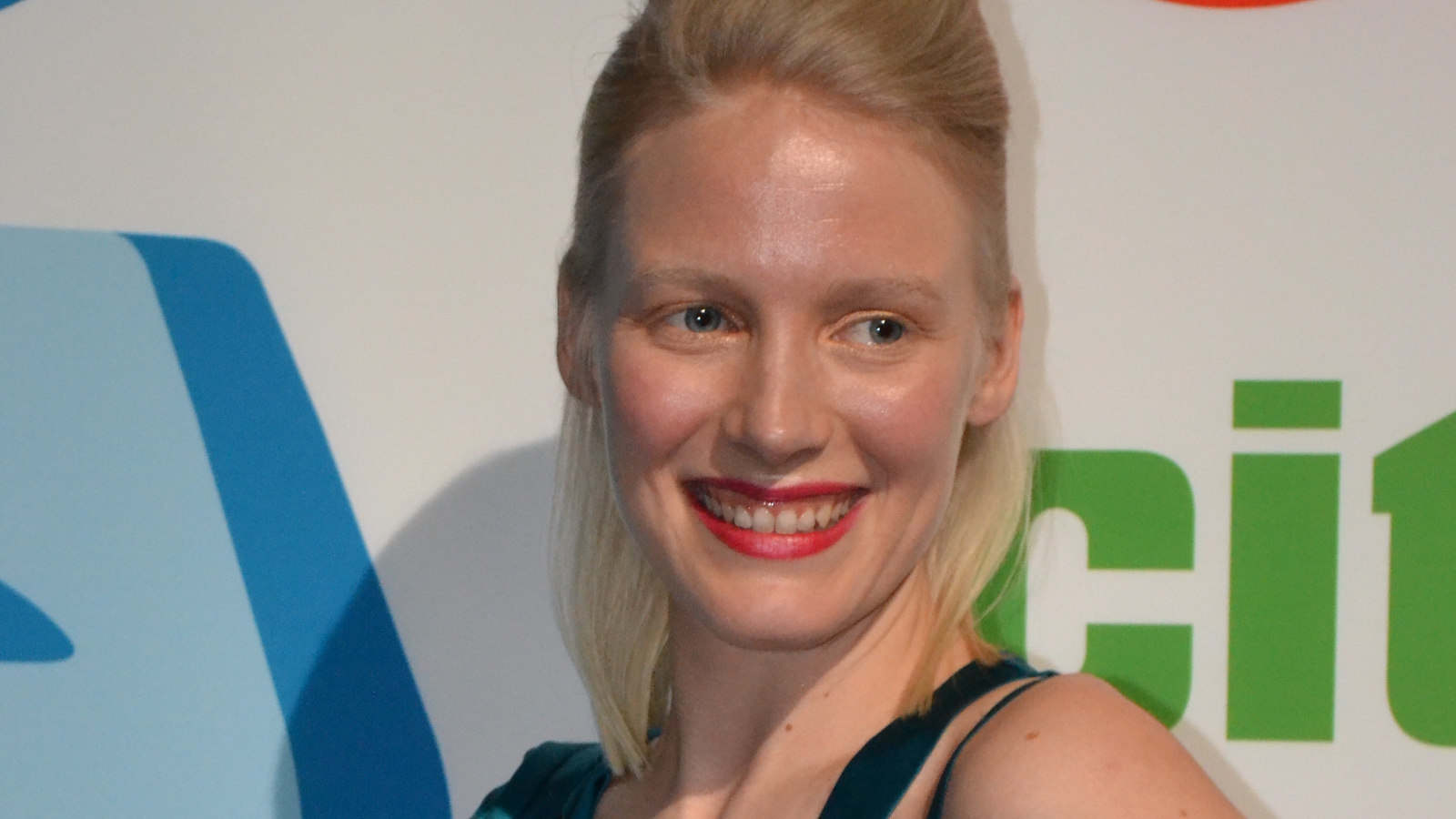 Kuvassa on Laura Birn kasvokuvassa ja hän poseeraa kuvaajille.  Taustalta näkyy oikealta vihreitä kirjaimia ja vasemmalta vihreitä kirjaimia.