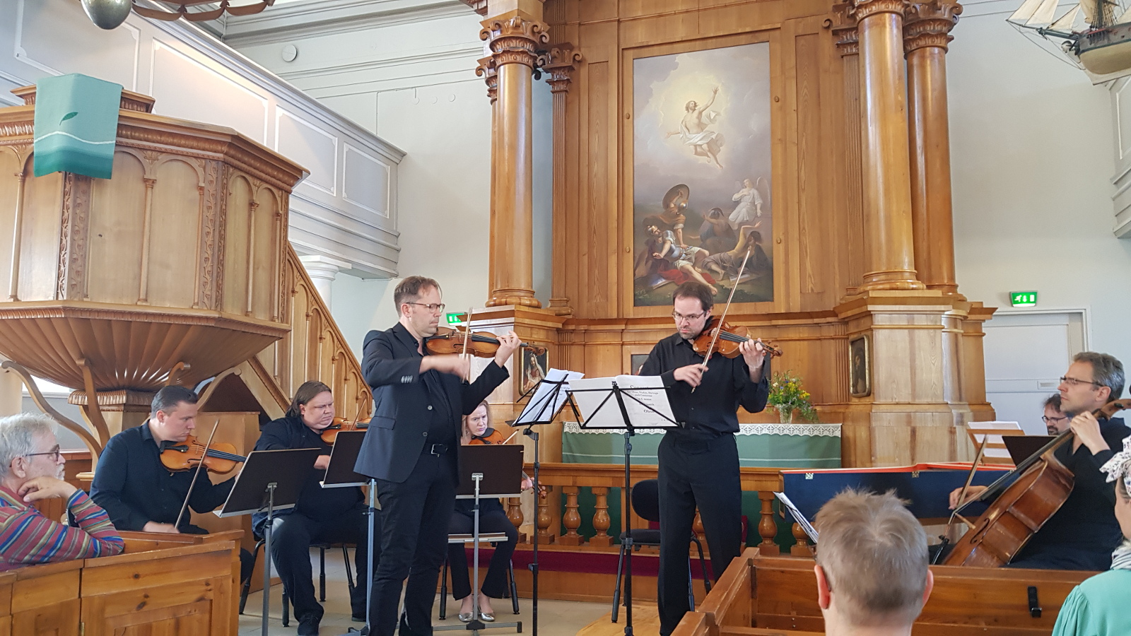 Kuvassa ovat soittamassa Kaakon Kamarimusiikin soittajat edessä soittamassa viulua vasemmalla Jukka Merjanen ja oikealla Petteri Iivonen. Taustalla on vaalean ruskeat pylväikot ja alttaritaulu sekä oikealla saarnastuoli.