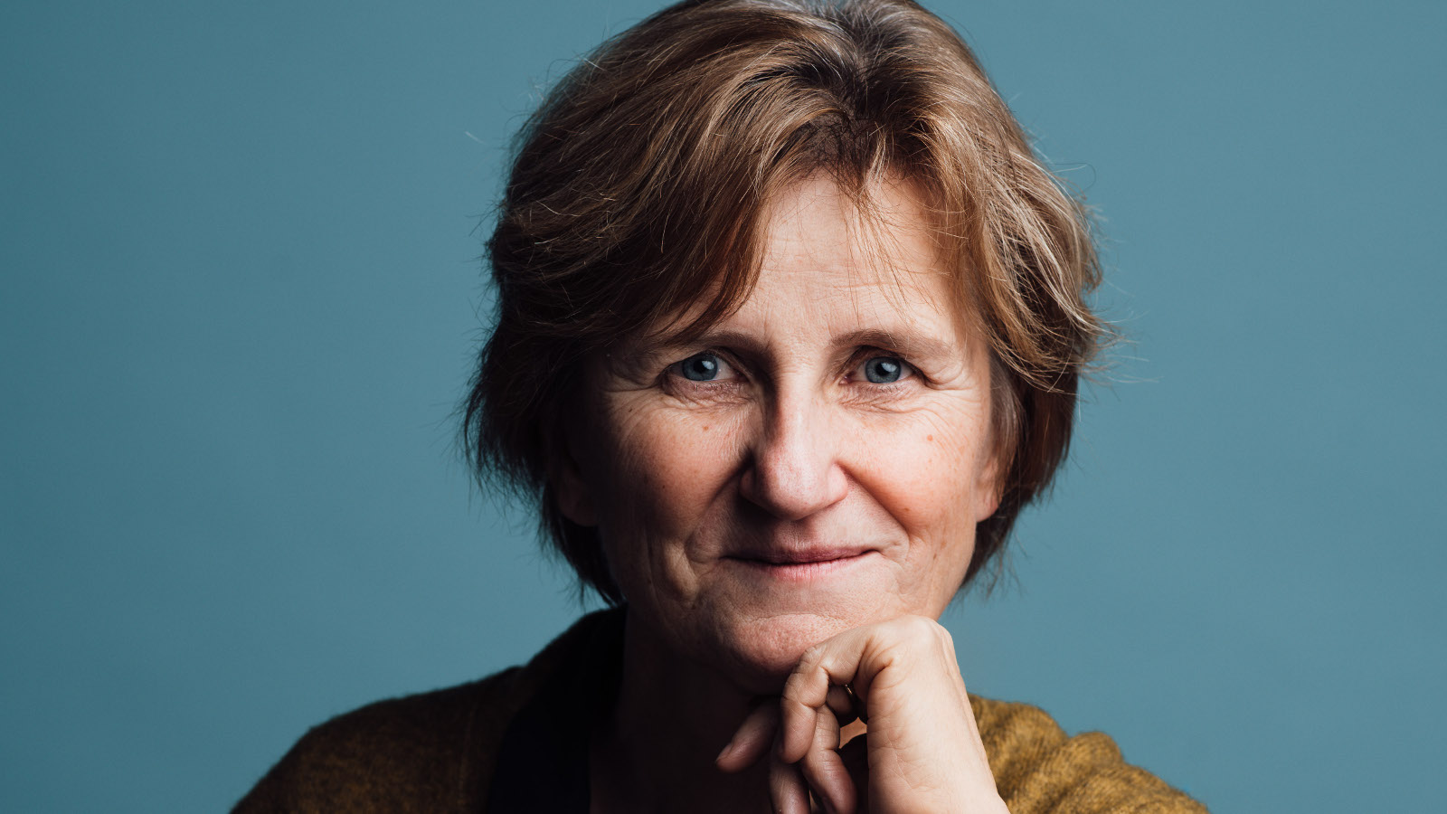 Kuvassa on Minna Lindgren kasvokuvassa ja hän nojaa vasemmalla kädellä leukaansa. Tausta on harmahtavan sininen. Kuva on osa kirjan kannesta.