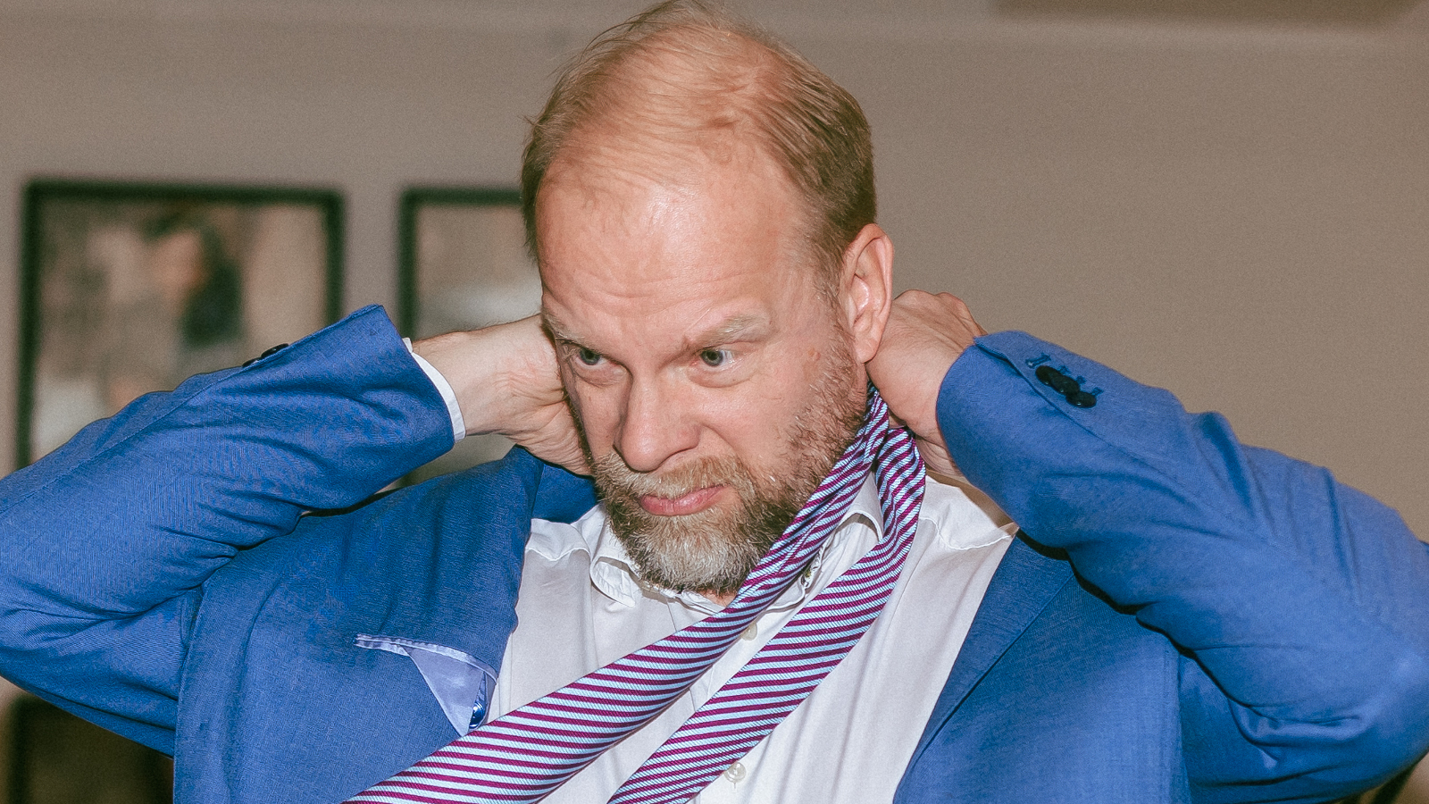 Kuvassa on Ville Myllyrinne vaalean sinisessä takissa ja hän kiskoo valkoista kravattia kaulastaan. Kuva on puolivartalokuvassa.