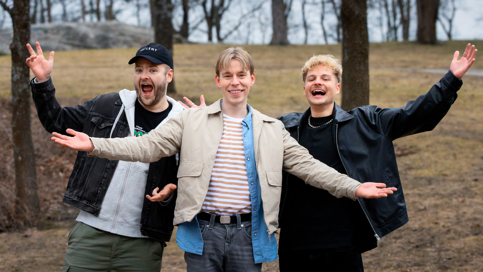 Kuvassa ovat kädet levitettynä sivulle vasemmalta Santeri Hänninen, Niko Meuronen ja Heny Weckström. Taustalla on mäki, jossa näkyy puunrunkoja. 