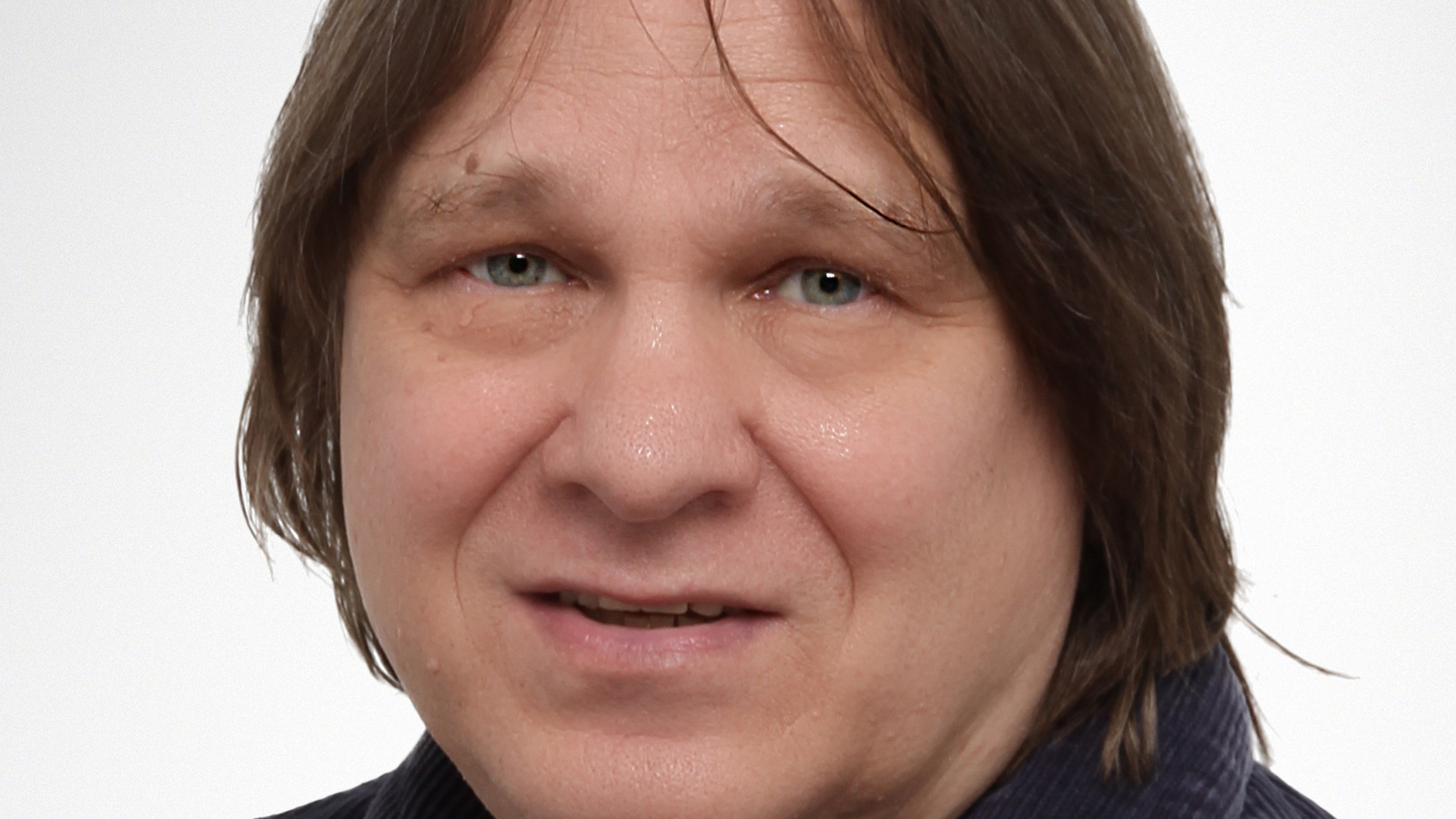 Kuvassa on Jukka Koskelainen kasvokuvassa ja hänellä on tumman ruskeat, puolipitkät hiukset.
