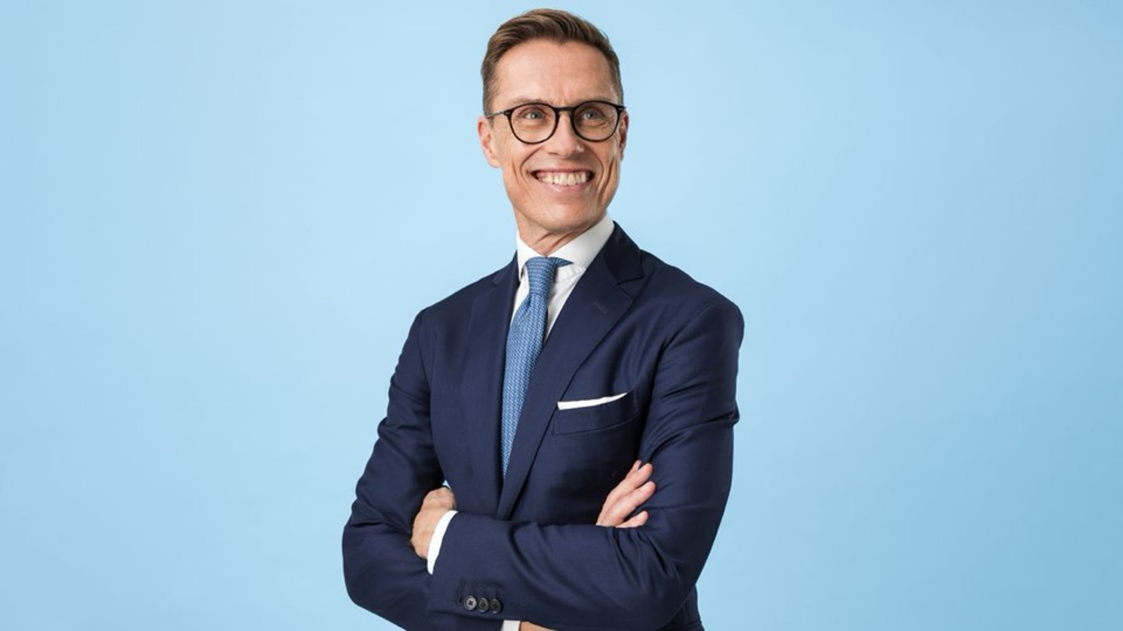 Kuvassa on Alexander Stubb puolivartalokuvassa. Hänellä on tumman sininen takki ja valkoinen paita sekä vaalean sininen kravatti päällään.  Tausta on vaalean sininen.