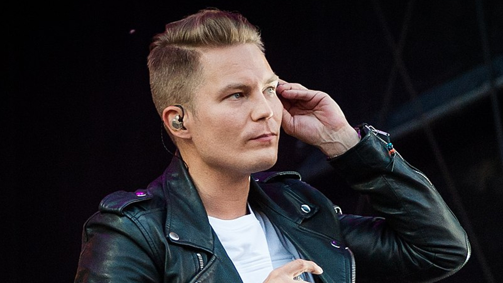 Kuvassa on puolittaisessa sivukuvassa Cheek, joka pitää vasemmalla kädellään kuuloketta korvallaan. Hänellä on lyhyet hiukset ja musta nahkatakki päällään.  Tausta on musta.