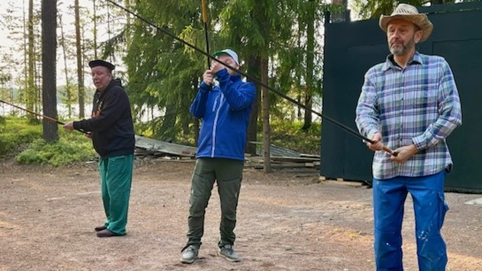 Kuvassa on kolme miestä seisomassa ja reunoilla olevat onvat onki kädessä. Heillä on hupparit ja verkkarit päällään.  Taustalla on metsää. 