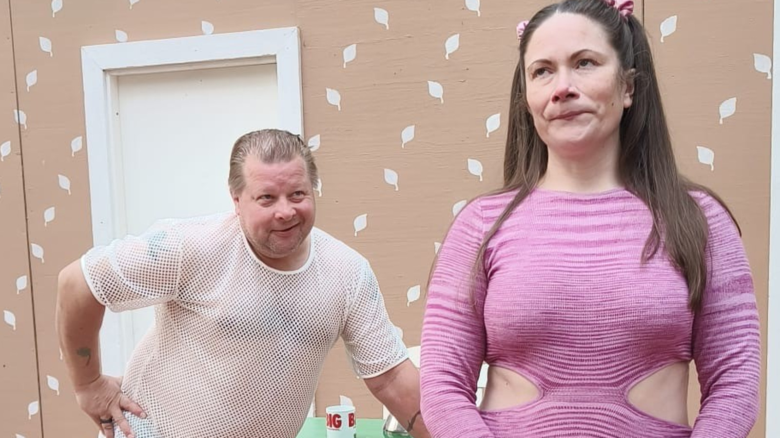 Kuvassa on vasemmalla mies valkoisessa verkkopaidassa ja nojaa eteenpäin. Edessä nainen kilassa paidassa.  Taustalla vaalean ruskeata tapettiseinää, jossa on valkoisia lehtiä.