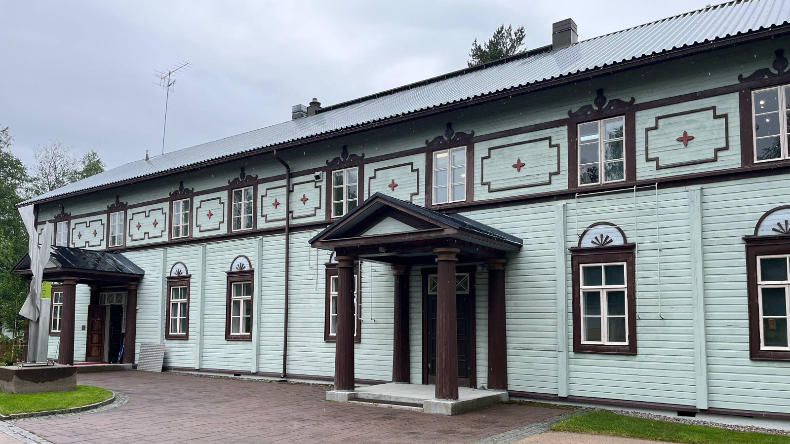 Kuvassa on Salmelan päärakennus, joka on turkoosi ja siinä on yläosassa ruskeaa koristelua ja niiden keskellä on ruskeat ikkunapuitteet.  Alhaalla on ruskeita isompia ikkunoita. Päädyssä ja keskellä on katokset.