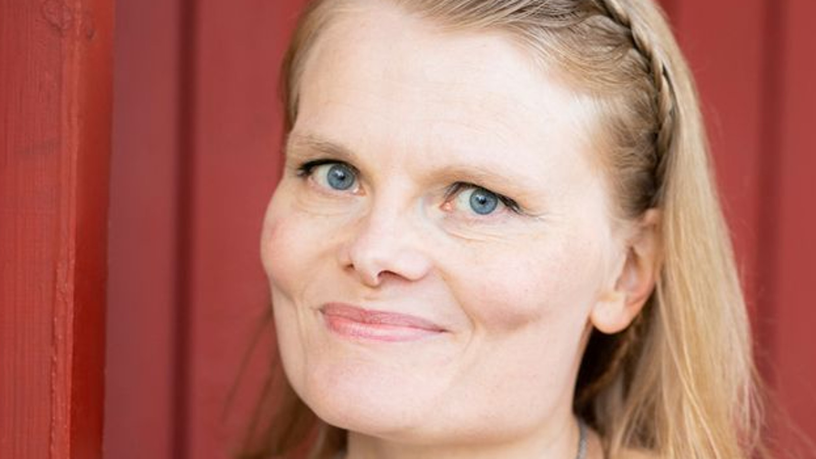 Kuvassa on Anneli Aakkula kasvokuvassa. Hänellä on vaaleat, pitkkät hiukset. Takana on punaista lautaseinää.