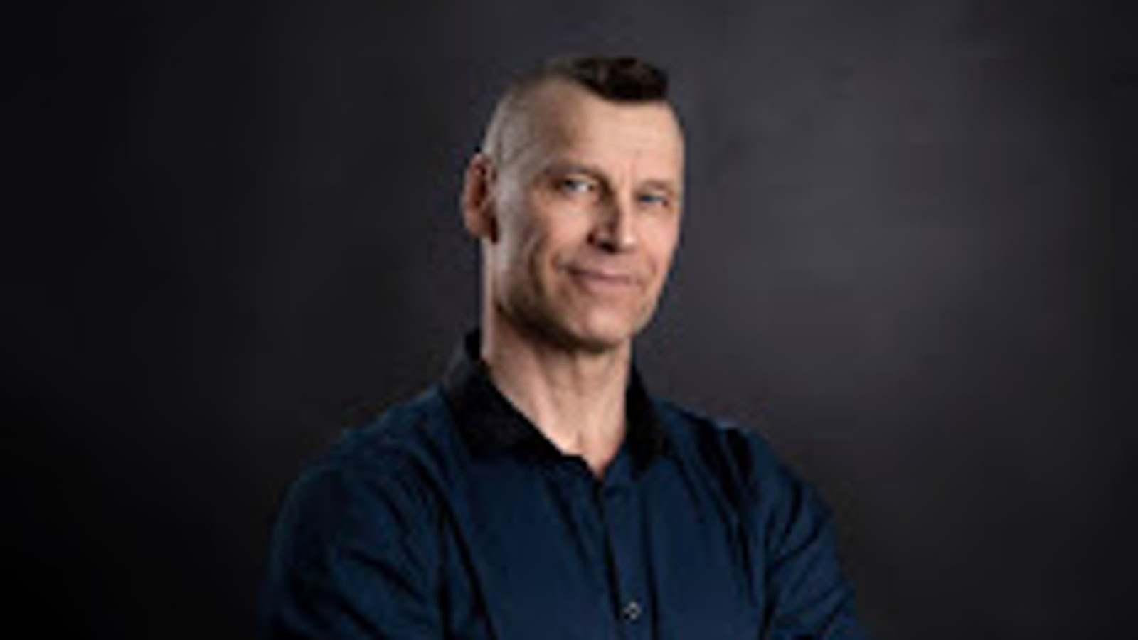 Kuvassa on Kari Valto ja hän seisoo puolivartalokuvassa sinisessä paidassa. Tausta on tumma.