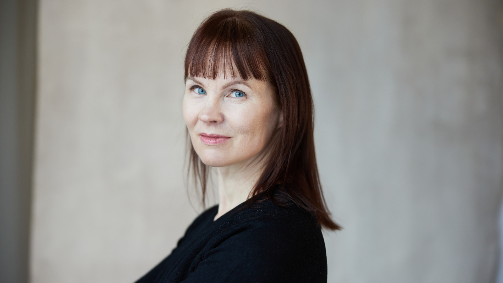 Kuvassa on Marisha Rasi-Koskinen puolivartalokuvassa ja hänellä on musta t-paita ja pitkät suorat hiukset. Tausta on harmaa.