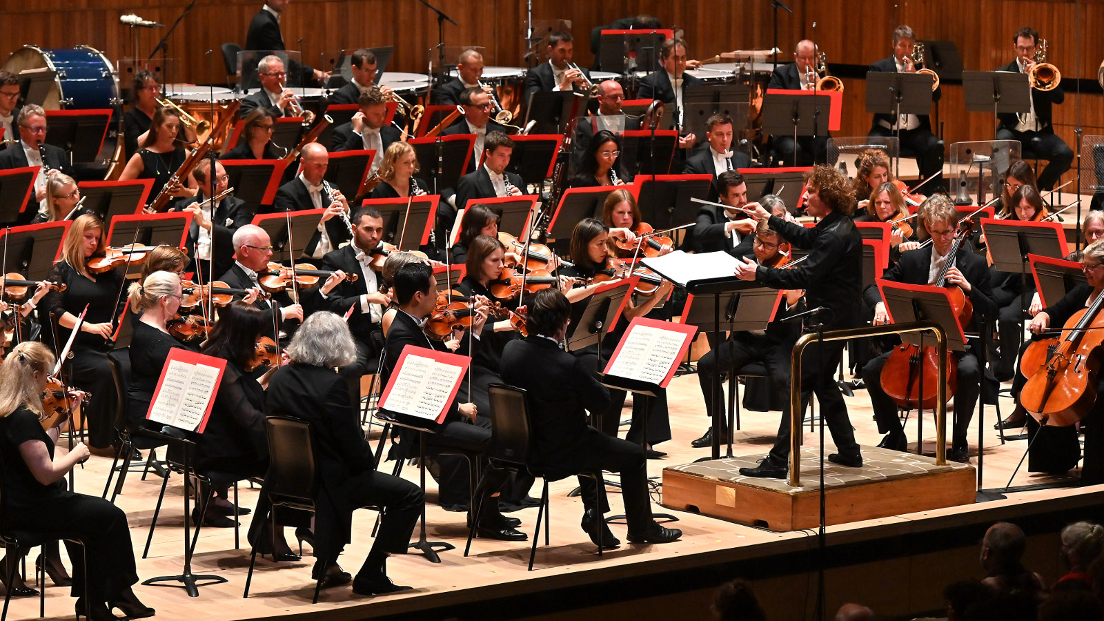 Kuvassa on Philharmonia Orchestra lavalla soittamassa tummissa puvuissa.