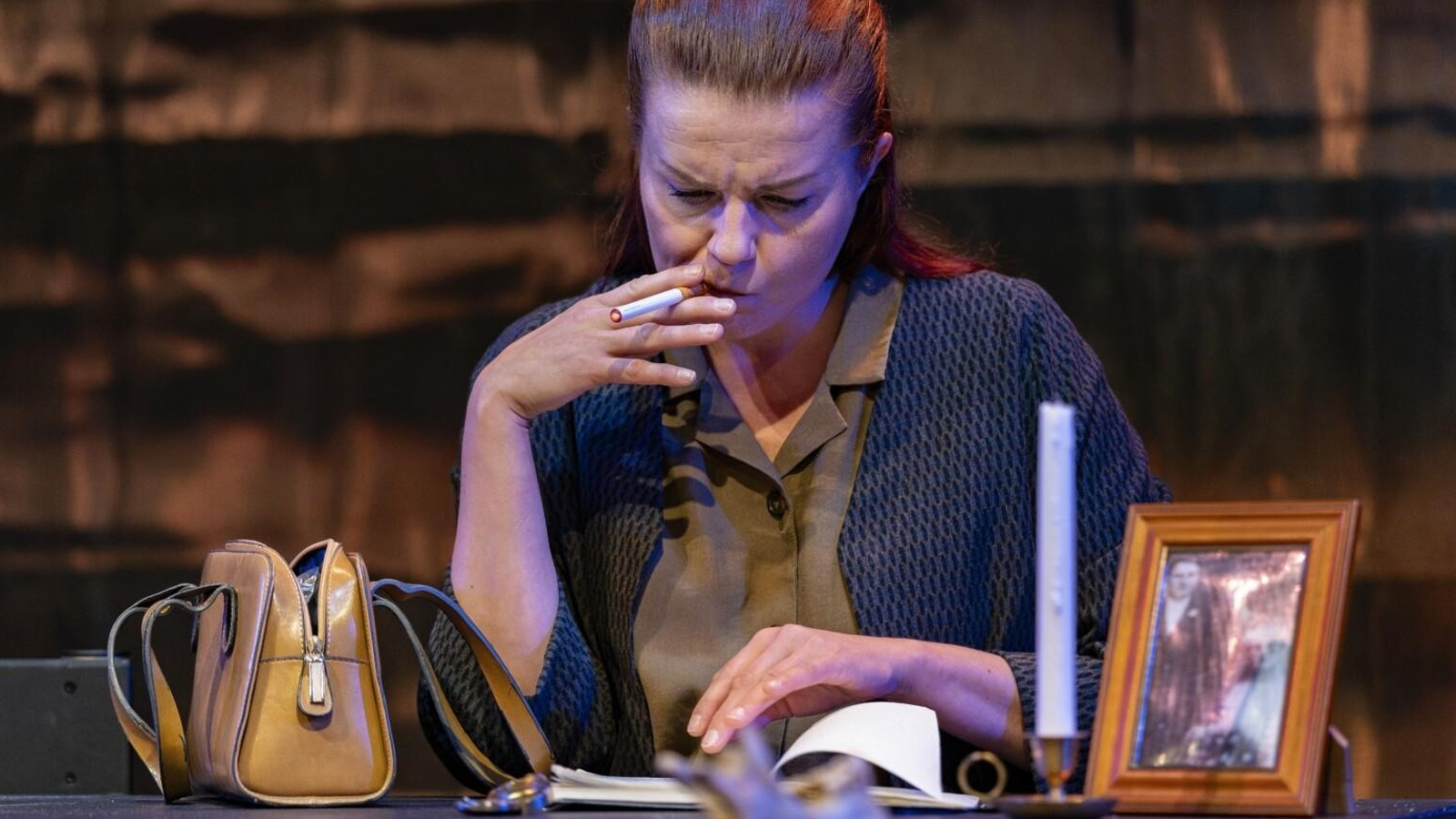 Kuvassa on nainen istumassa ja lukemassa kirjaa.  Hänellä on vihreän harmaa pusero päällään ja hän tupakoi. Vasemmalla vieressä pöydällä on vihertävä käsilaukku.