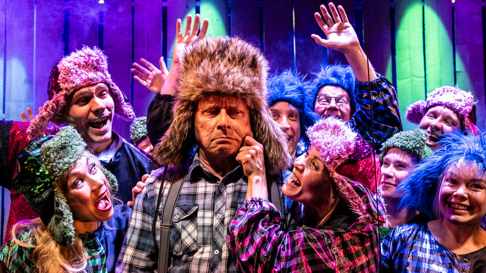 Kuvassa on Jukka-Pekka Löhönen keskellä karvahatussa ja ruutupaidassa. Häntä nipistää poskeen Tiina Räsänen vasemmalla kädellään ja hänellä on myös karvahattu. Ympärillä on monia henkilöitä ja kaikilla on karvahattu päässään. He virnistelevät ympärillään Kihlströmin esittämälle Mielensäpahoittajalle.