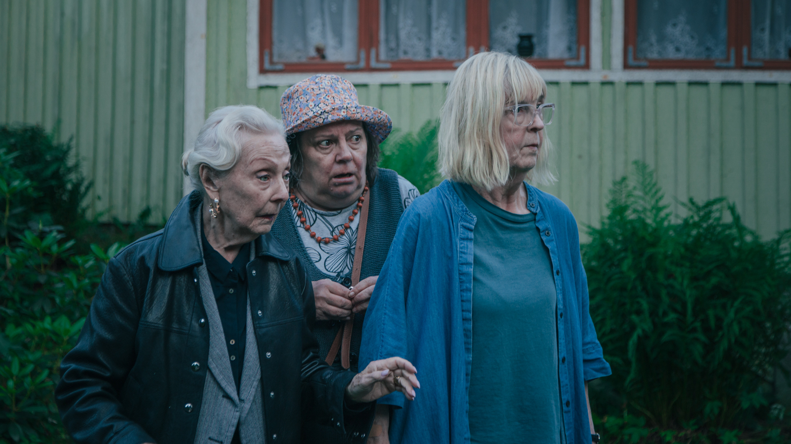 Kuvassa ovat vasemmalta SEela Sella tummassa takissa vieressään Leena Uotila pikässä sinisessä farkkutakissa ja sinisessä puserossa. Heidän välissään kurkkii Sanna-Kaisa Palo harmaan kirjavassa hatussa. Taustalla on vaalean vihreä talo, jossa on ikkunassa ruskeat karmit.