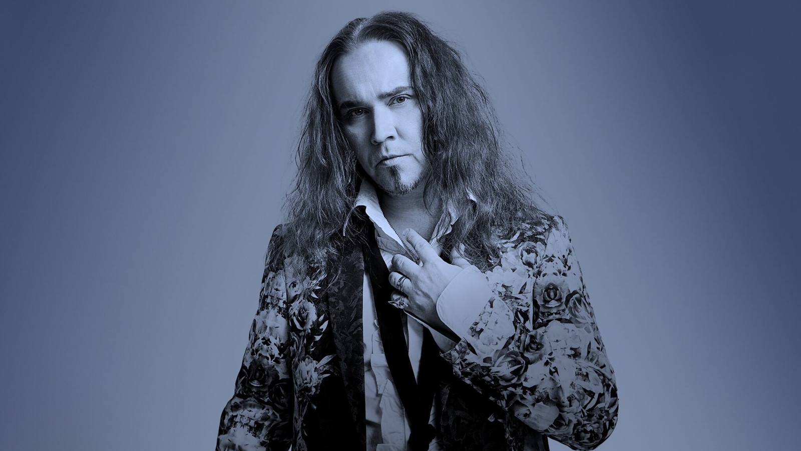 Kuvassa on Jarkko Ahola keskellä ja hänellä on kirjavasti kuvioitu takki päällään. Hänellä on pitkät, kiharat hiukset. Tausta ja kuvan sävy on sini-harmaa.
