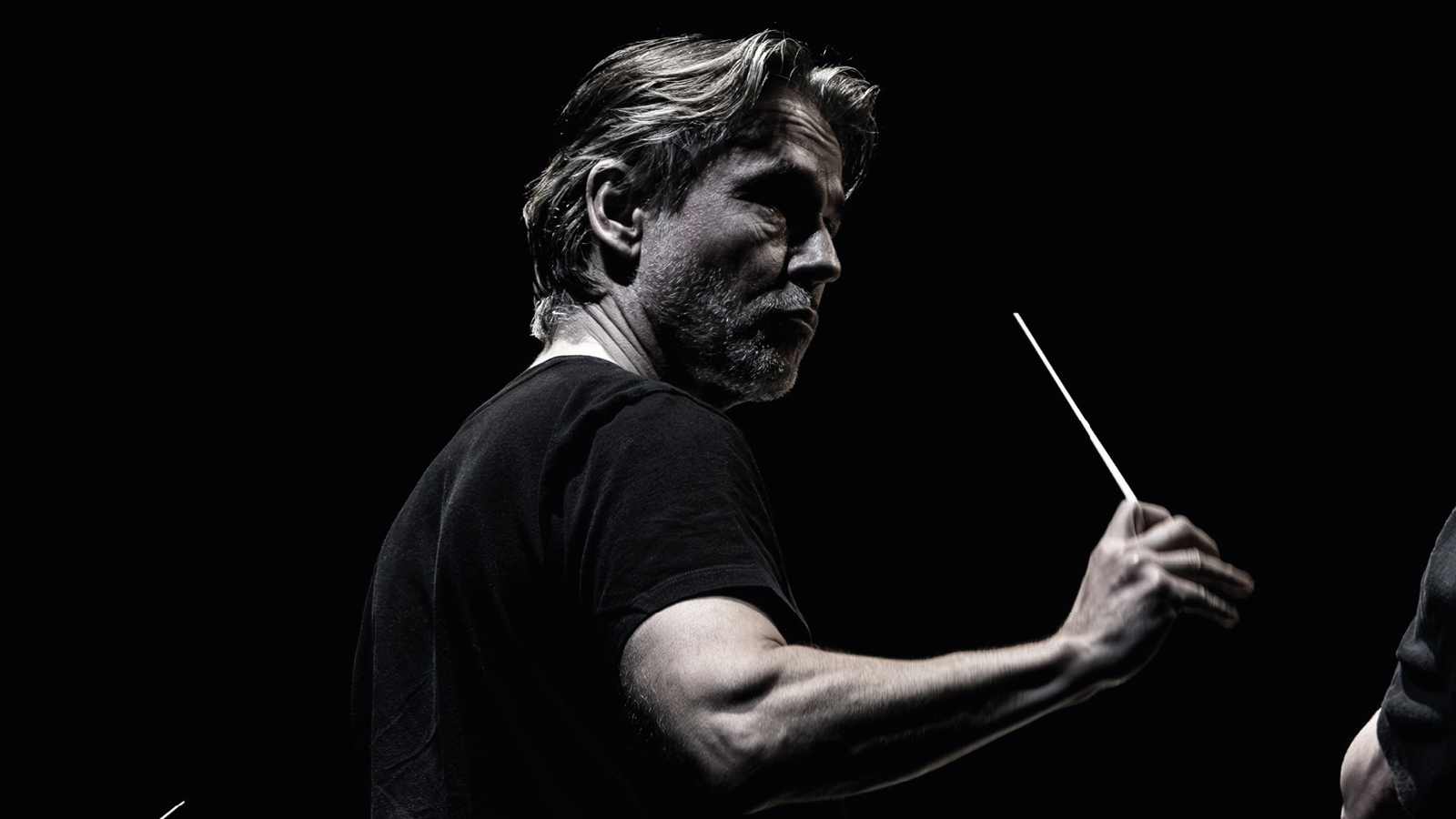 Kuvassa on Esa-Pekka Salonen puolivartalokuvassa johtamassa orkesteria. Hänellä on tahtipuikko kädessään ja hänellä on musta t-paita päällään. Kuvan tausta on musta ja kuva on musta-valkoinen. Kuva on osa kirjan kantta.