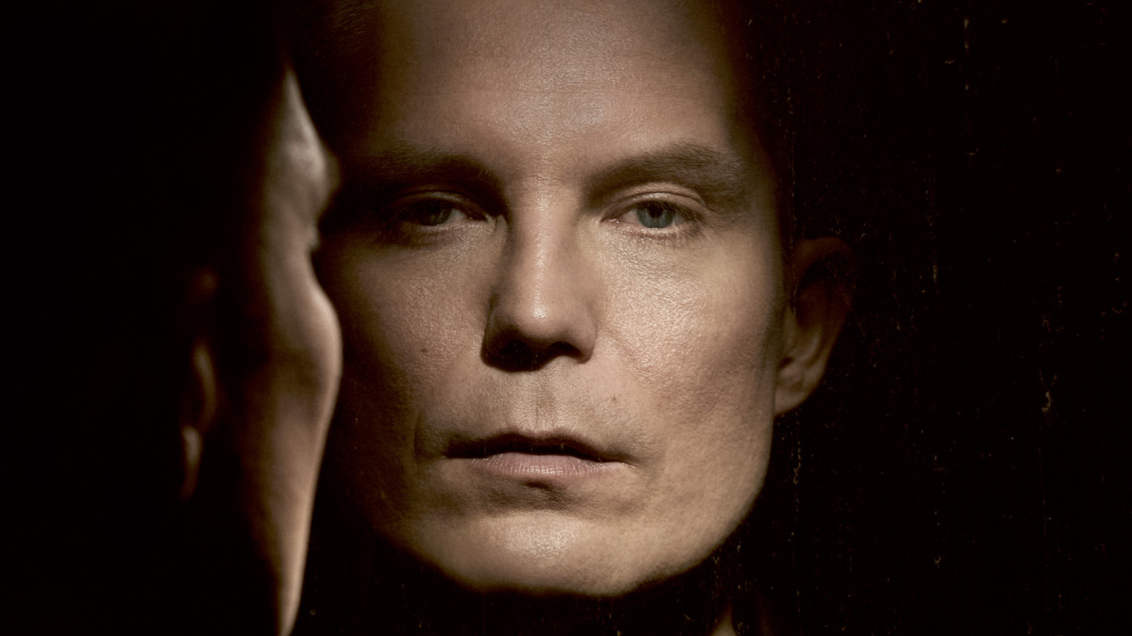 Kuvassa on Jari Tiihosen kasvot ja vasemmalla on sivukuva kasvoista kohti kasvokuvaa. Kuva on musta-valkoinen ja hieman ruskehtava. Tausta on tumma ja kuva on osa kirjan kannesta.