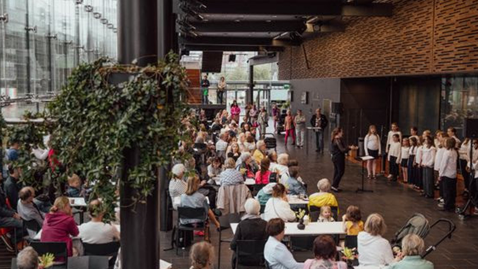 Kuvassa on Musiikkitalossa yleisöä laulamassa ja oikealla edessä on valkoisissa puseroissa nuorten kuoro laulamassa.